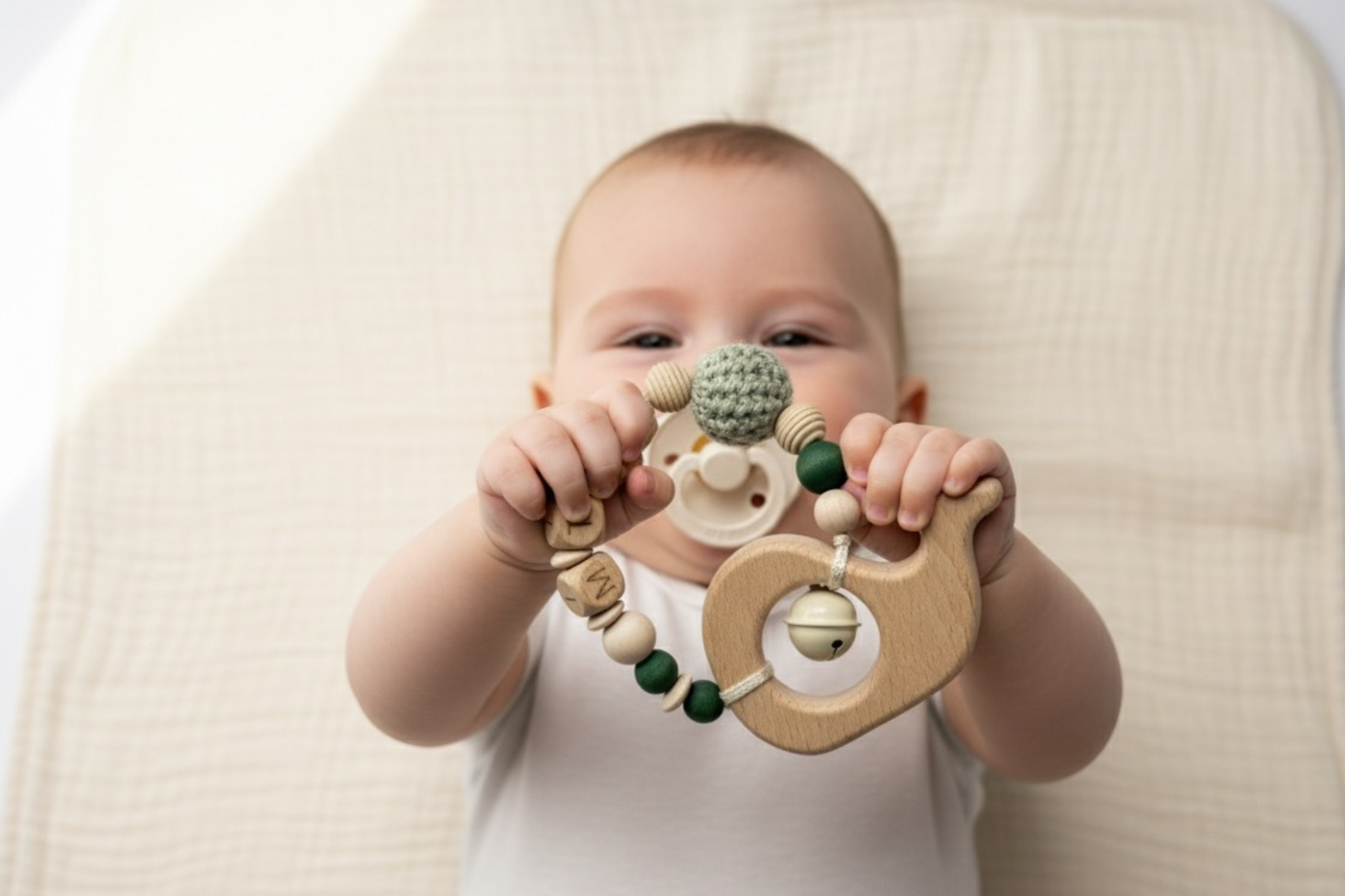 Baby hält einen Greifring Beißring aus Holz und Silikon in der Hand und erkundet ihn spielerisch.