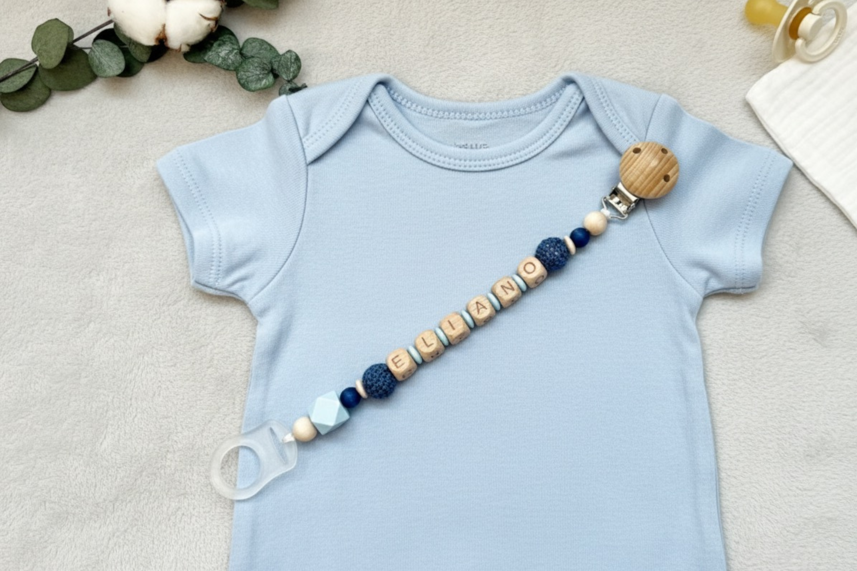 Personalisierte Schnullerkette aus Holz und Silikon, befestigt an einem Babybody.